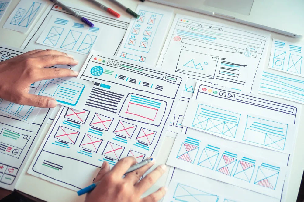 Hands reviewing interface sketches and a workflow plan on paper